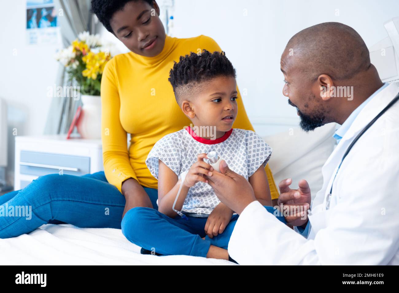 African american male doctor showing inhaler to boy patient, with ...