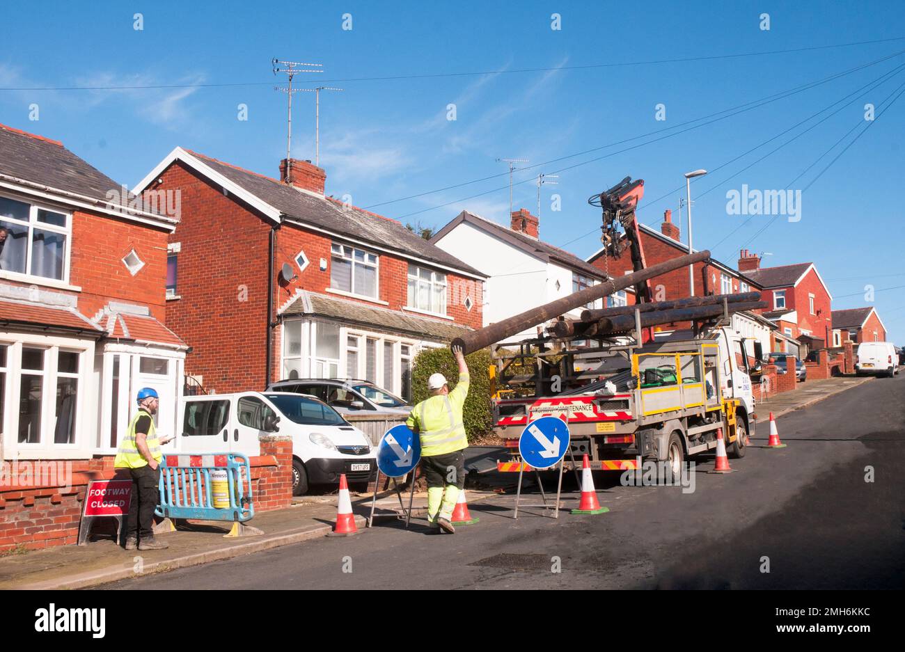 Cones signs and barrier around workmen erecting pole to carry overhead  fibre optic cable for G6 Broudband Internet WI FI network connections Stock Photo