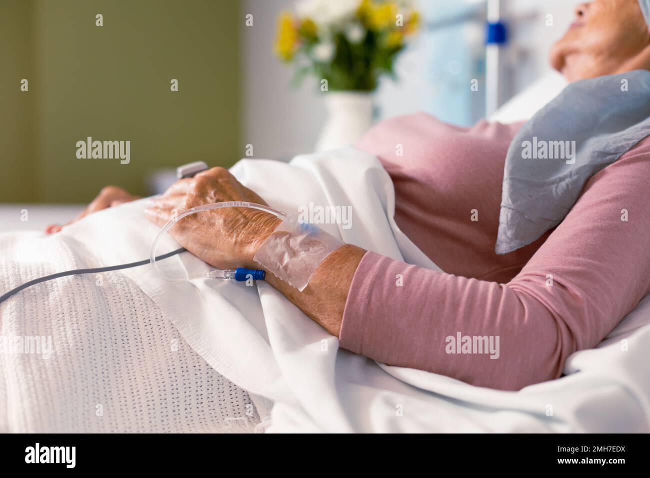 Senior caucasian female cancer patient wearing head scarf lying in bed with drip at hospital Stock Photo