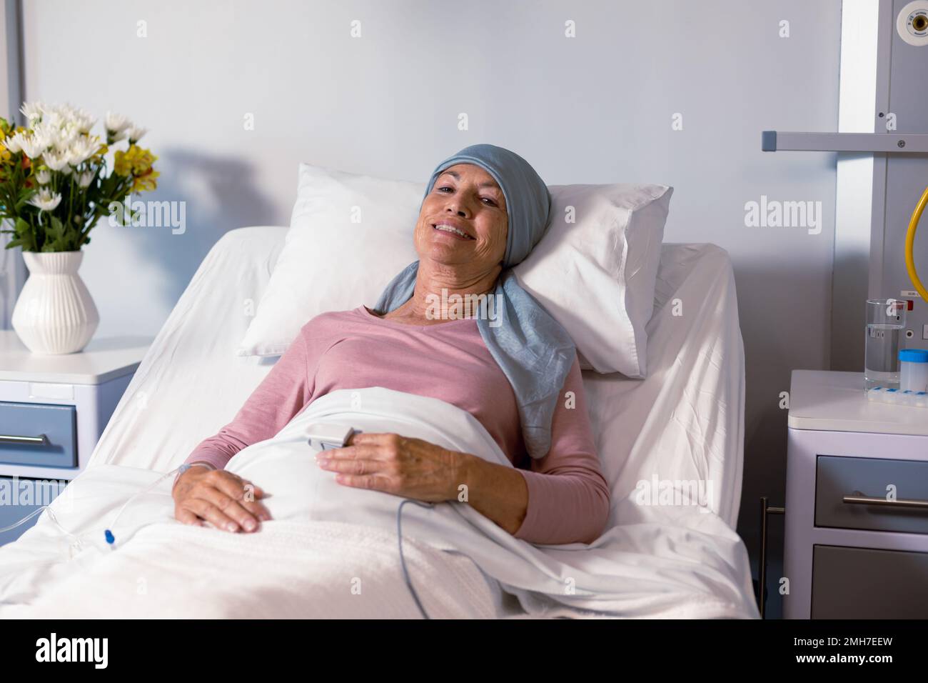 Smiling senior caucasian female cancer patient wearing head scarf lying in bed at hospital Stock Photo