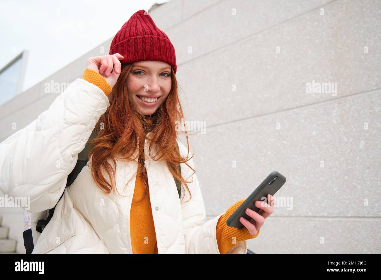 Joyful girl tourist looks at mobile phone, texts message on smartphone social media application, walks around city, looks for sightseeing on mobile Stock Photo