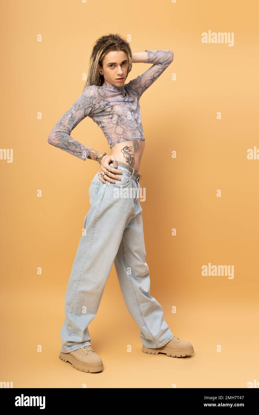 Full length of tattooed nonbinary person looking at camera on yellow background,stock image Stock Photo