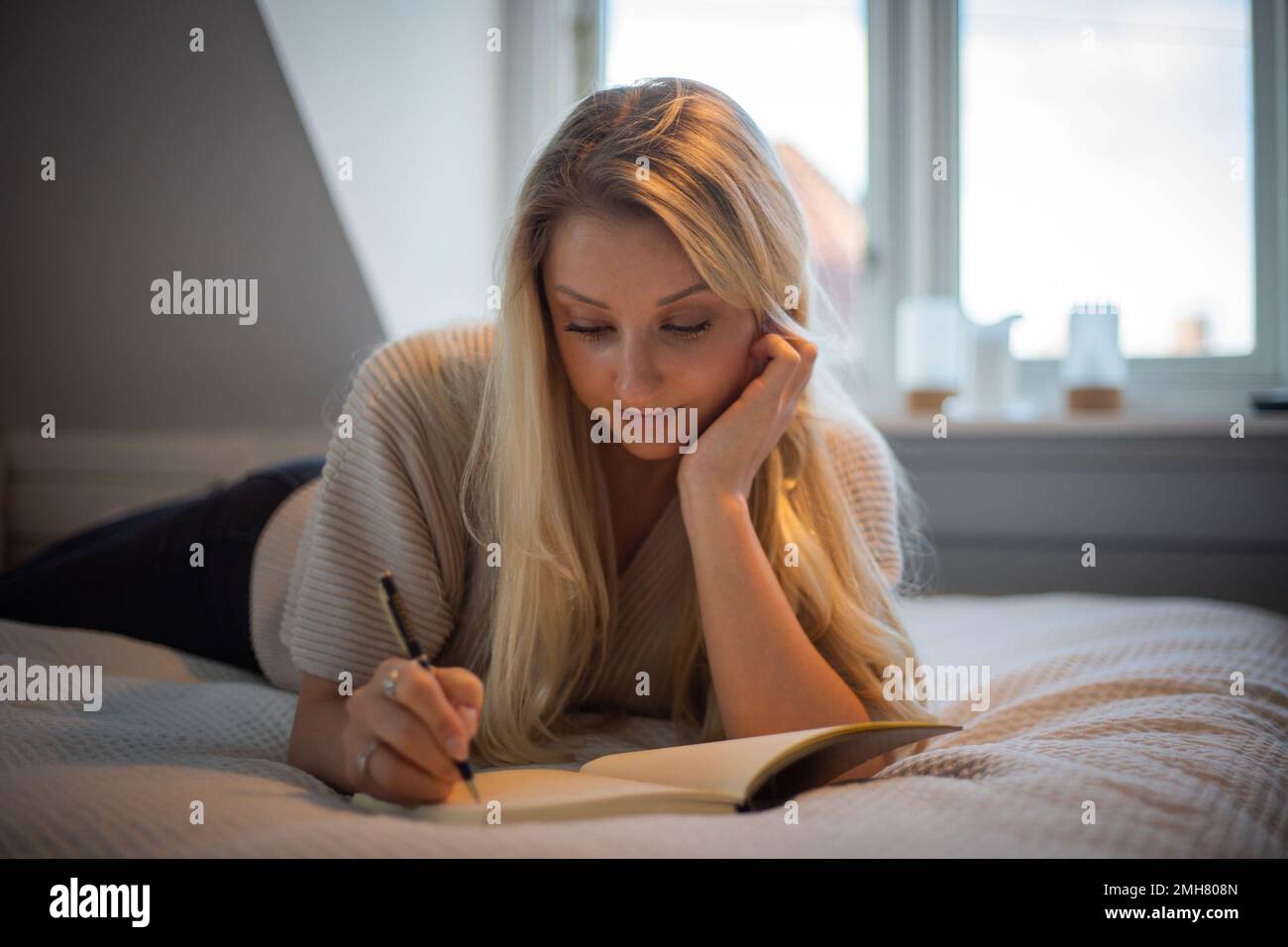 An attractive girl lying on her bed writes in her personal diary Stock Photo