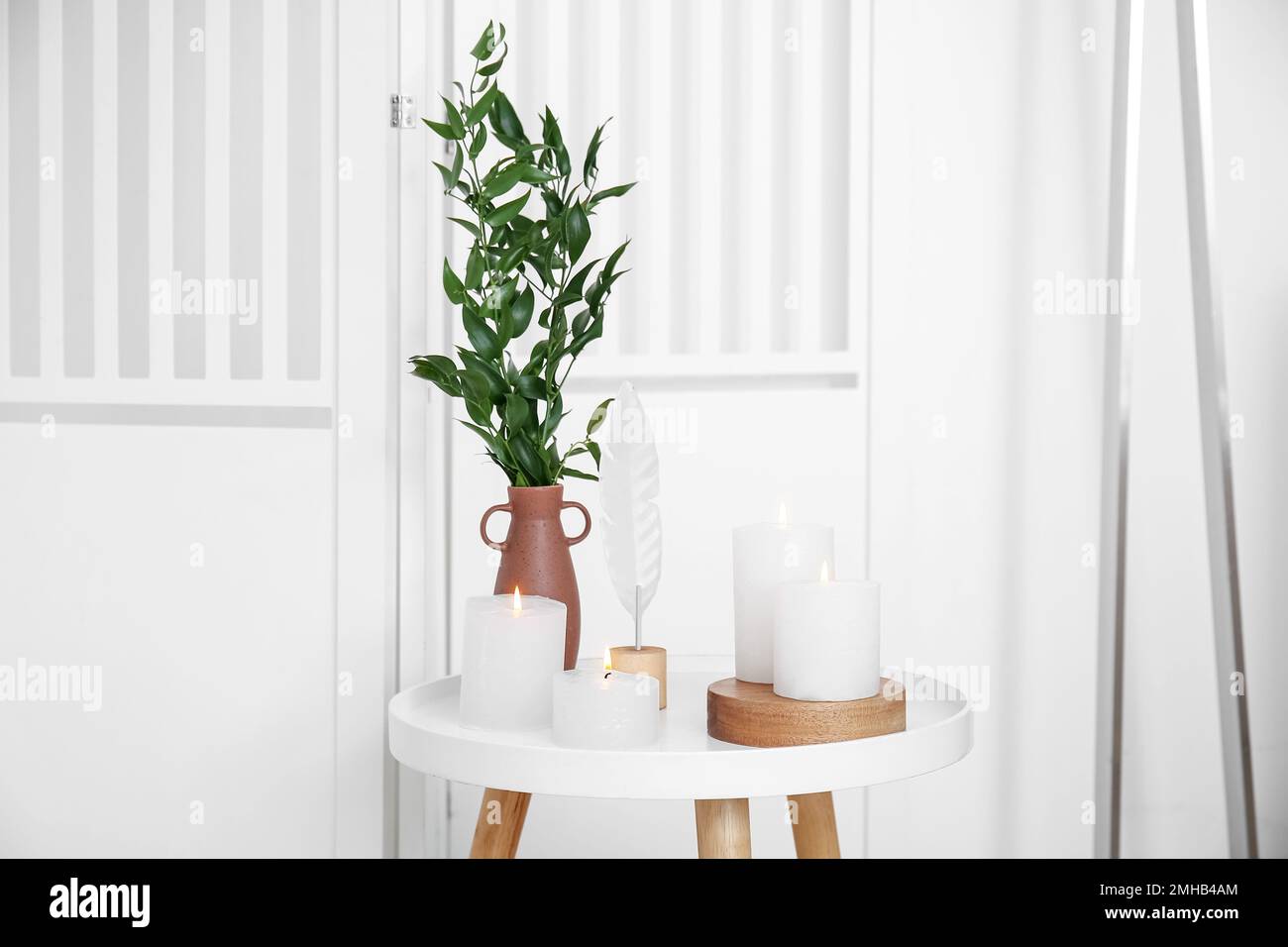 Burning candle and houseplant on end table near folding screen Stock