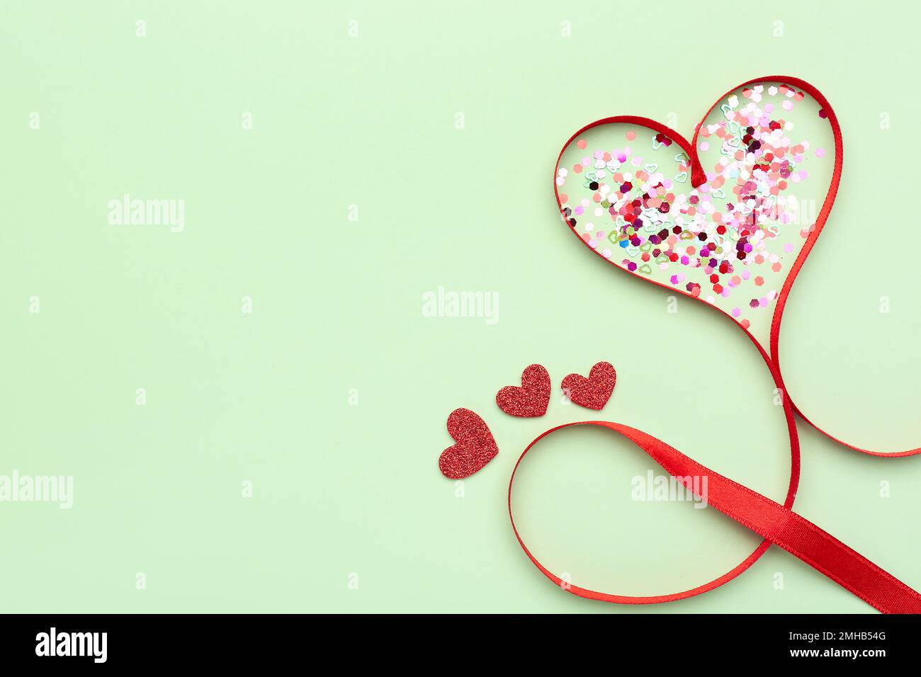 Sequins and heart made of red satin ribbon on green background ...
