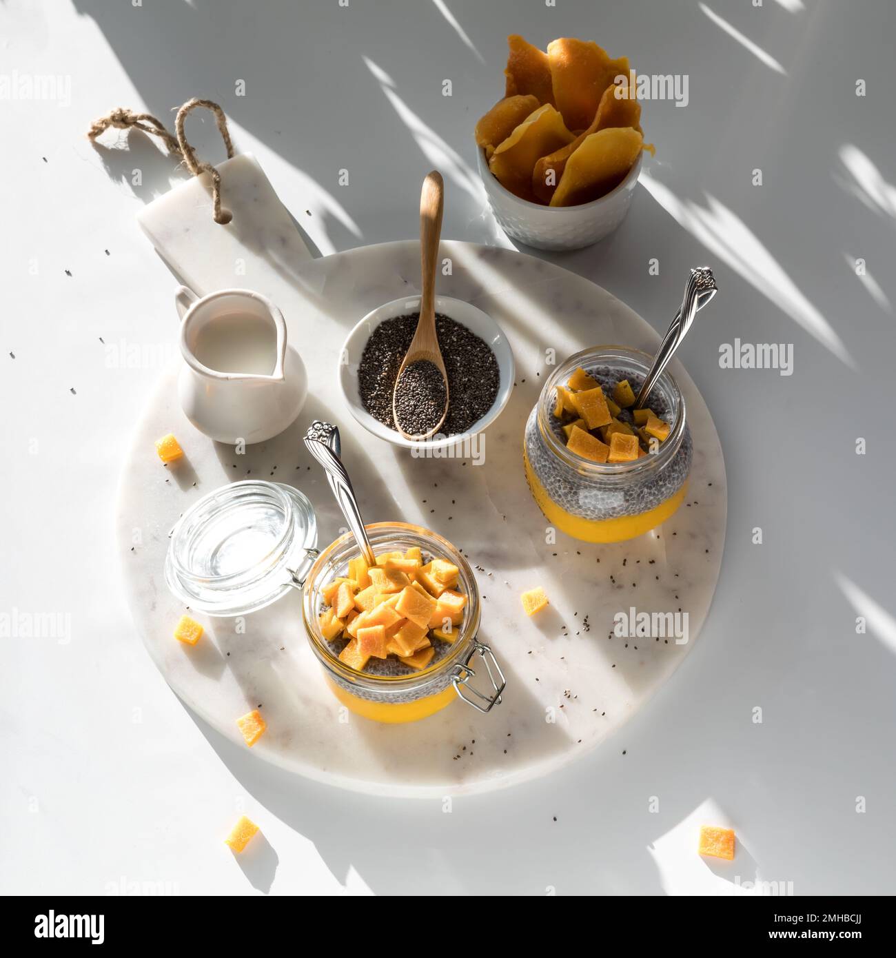 Mango chia pudding snacks on a white marble slab in shadowy bright sunlight Stock Photo