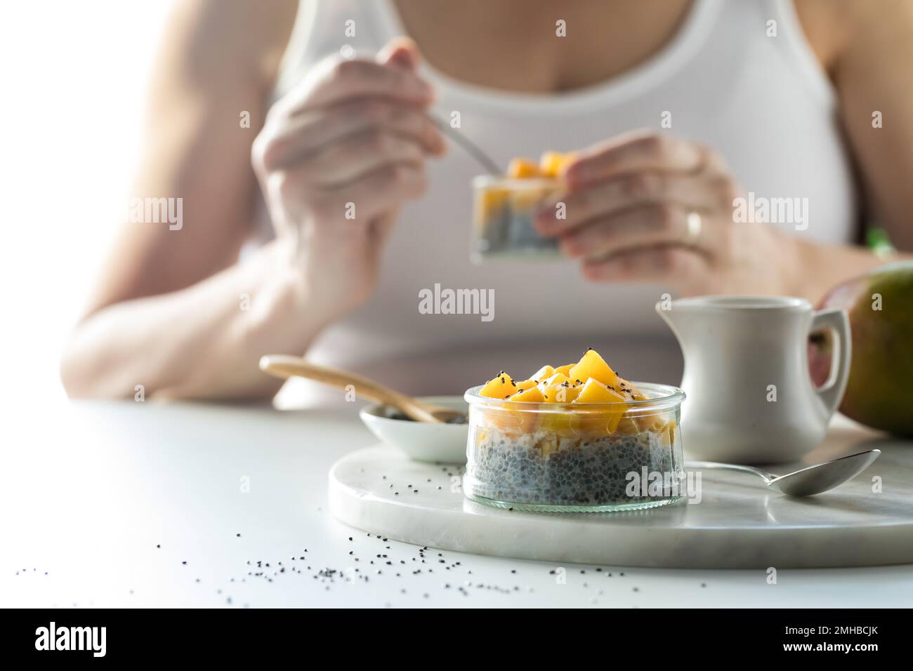 A close up view of a mango chia pudding snack with a woman eating one in behind. Stock Photo