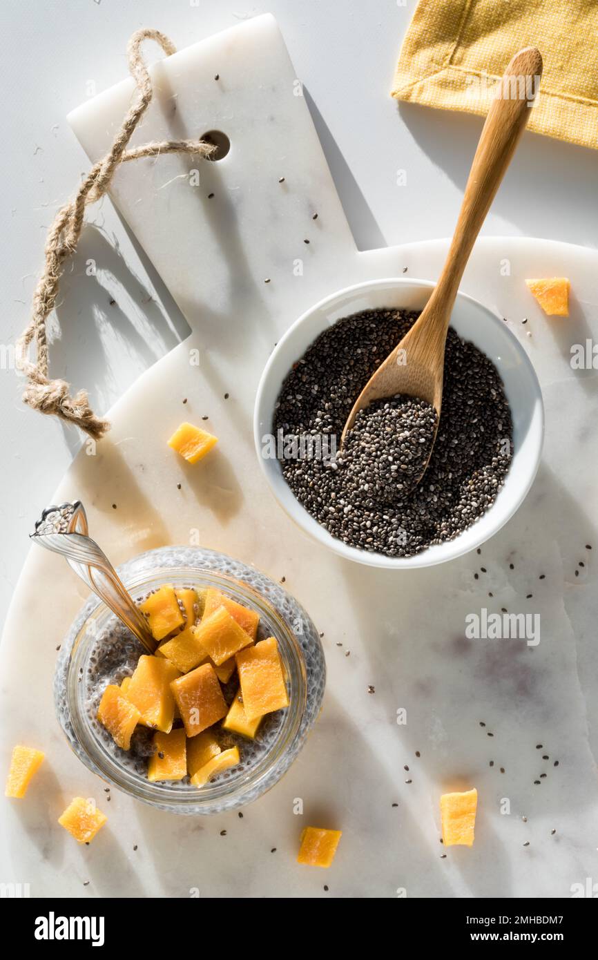 A mango chia pudding parfait on a marble board with a bowl of chia seeds. Stock Photo
