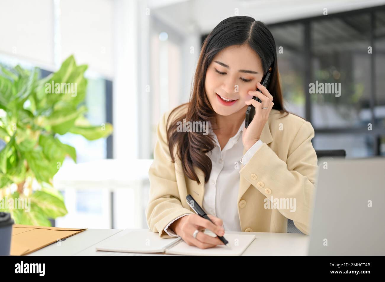 Attractive millennial Asian businesswoman taking notes on her notebook ...