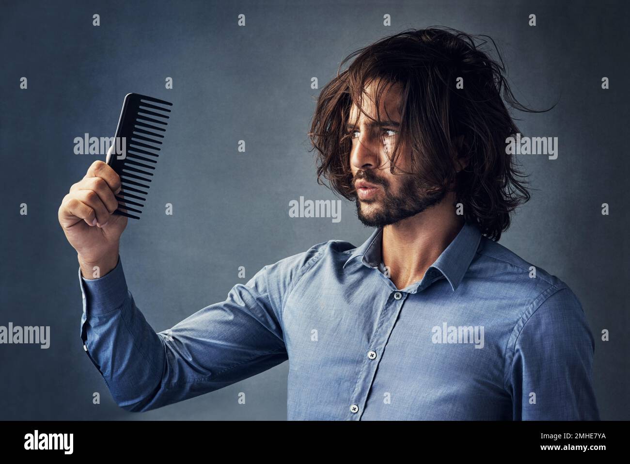 Youre supposed to be helping me. Studio shot of a handsome young man looking at his comb while brushing his hair against a grey background. Stock Photo