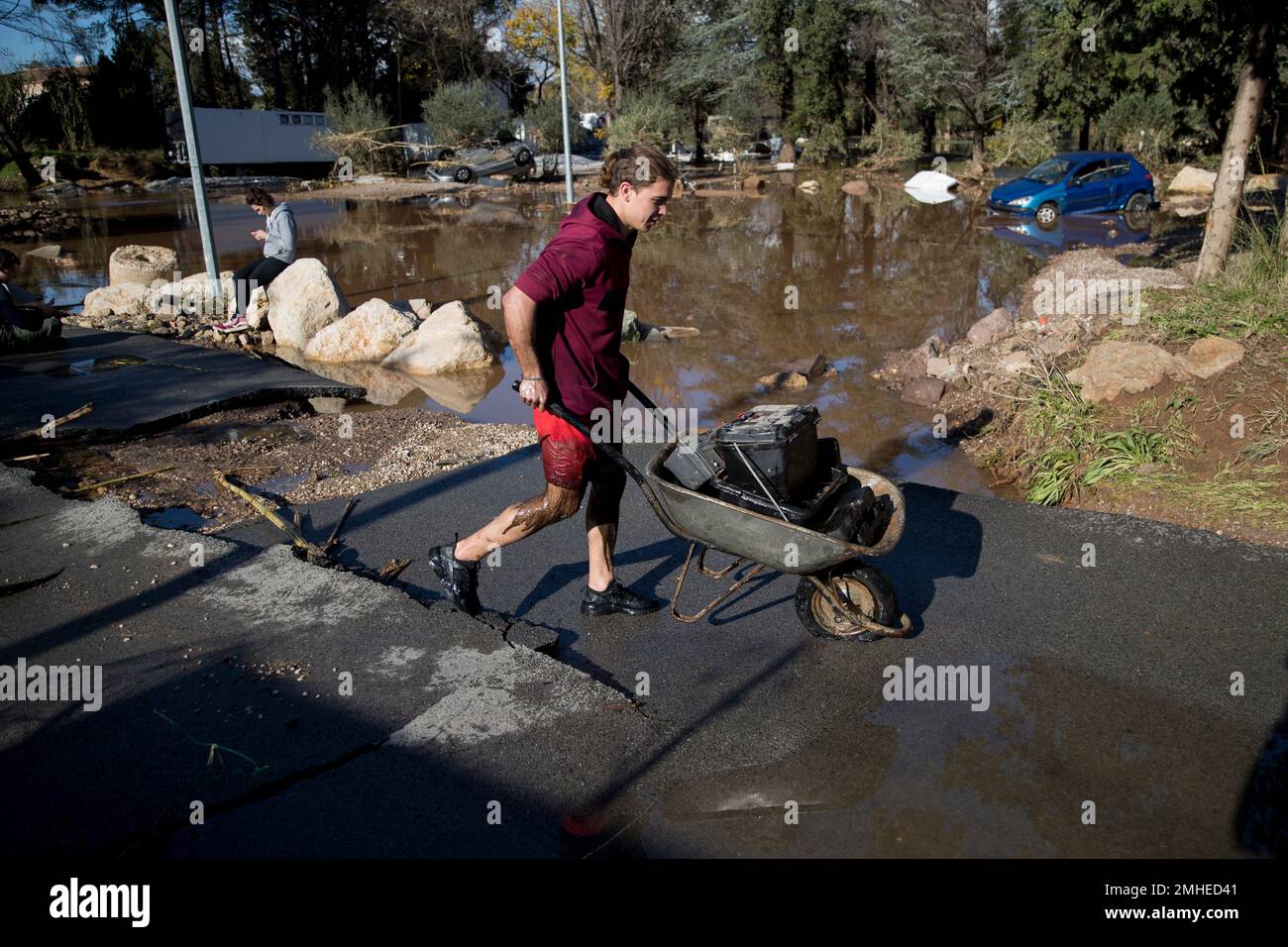 A man carries supplies in a wheelbarrow along a road destroyed by ...