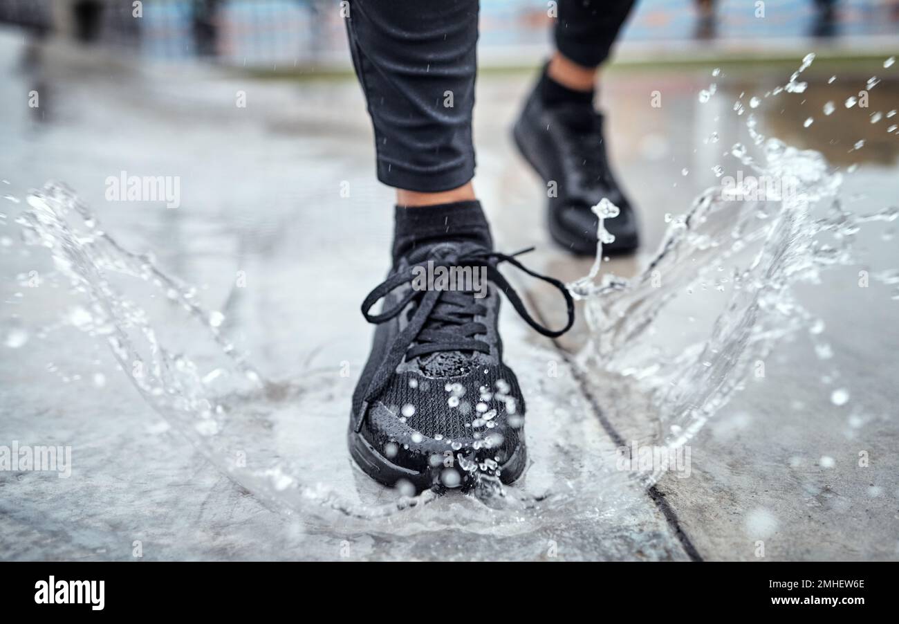 Shoes of person running in the rain, feet splash water in puddle and