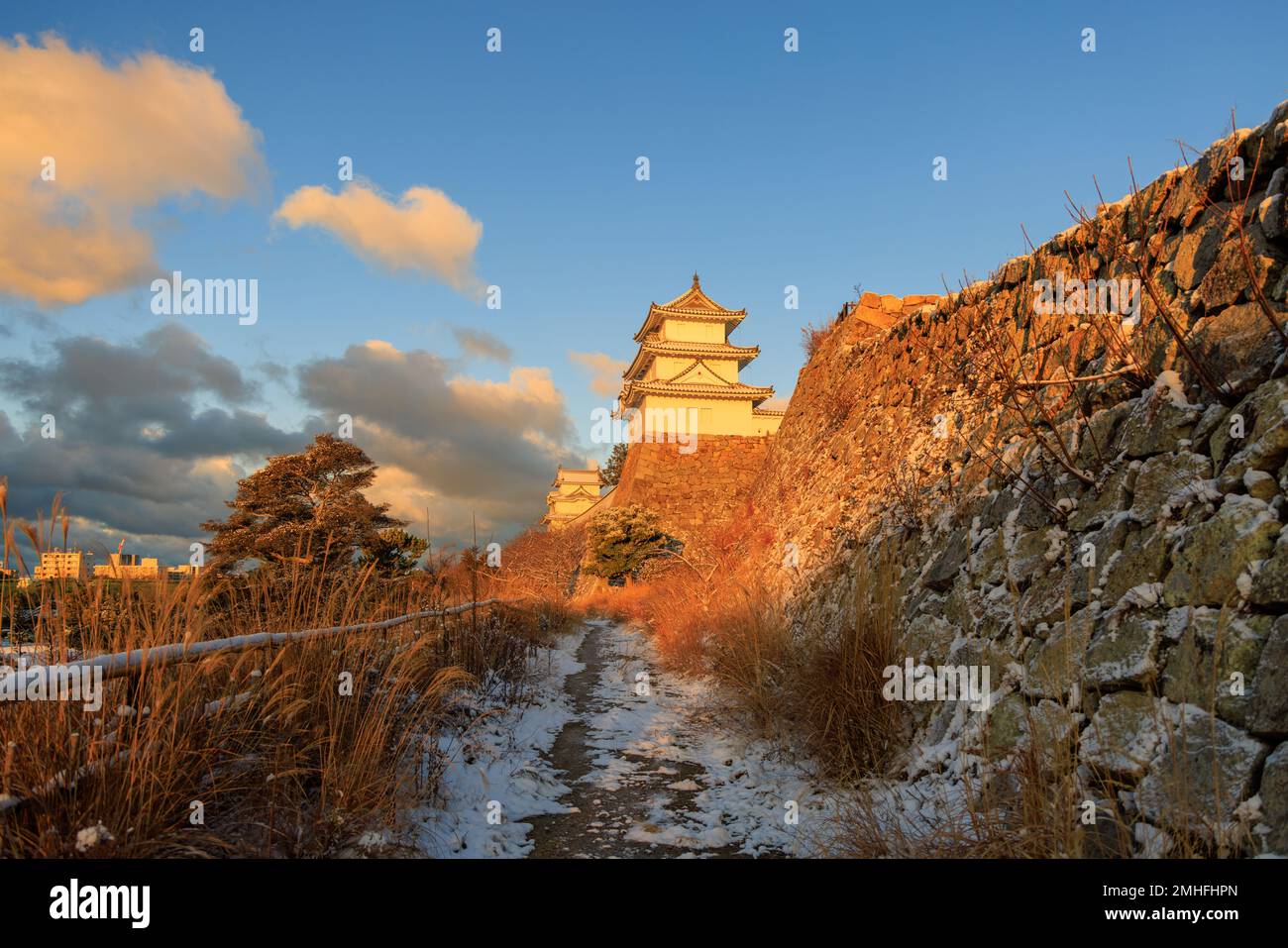 Snow on path by snow wall to historic Japanese castle in golden morning light Stock Photo