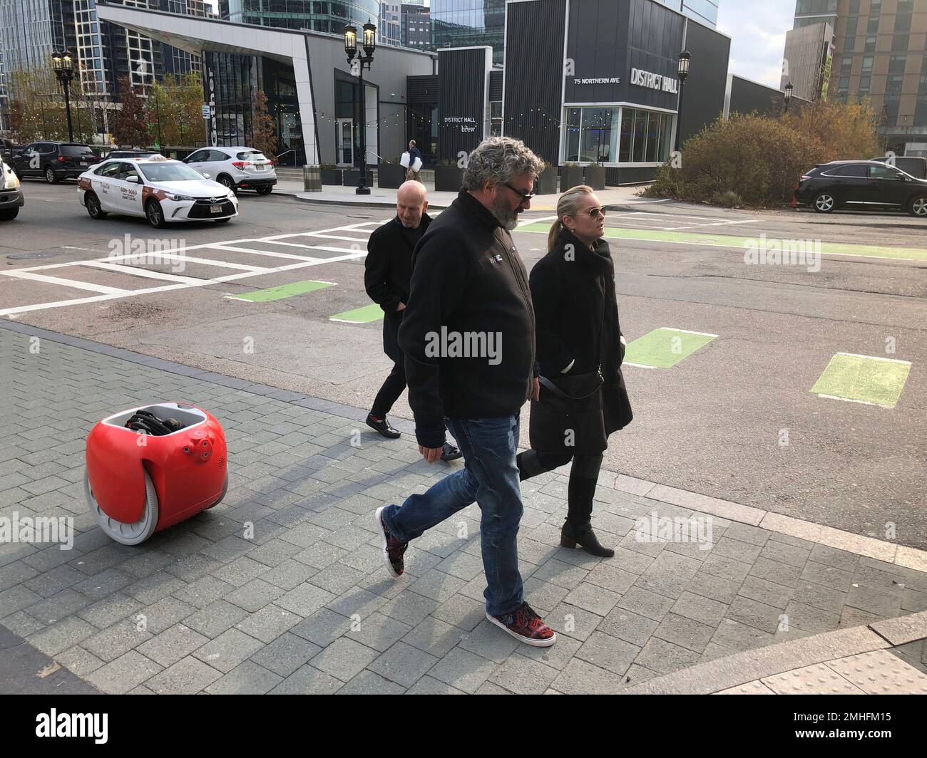 Piaggio Fast Forward CEO Greg Lynn, center, is followed by his company's  Gita carrier robot as he crosses a street on Monday, Nov. 11, in Boston.  The two-wheeled machine is carrying a