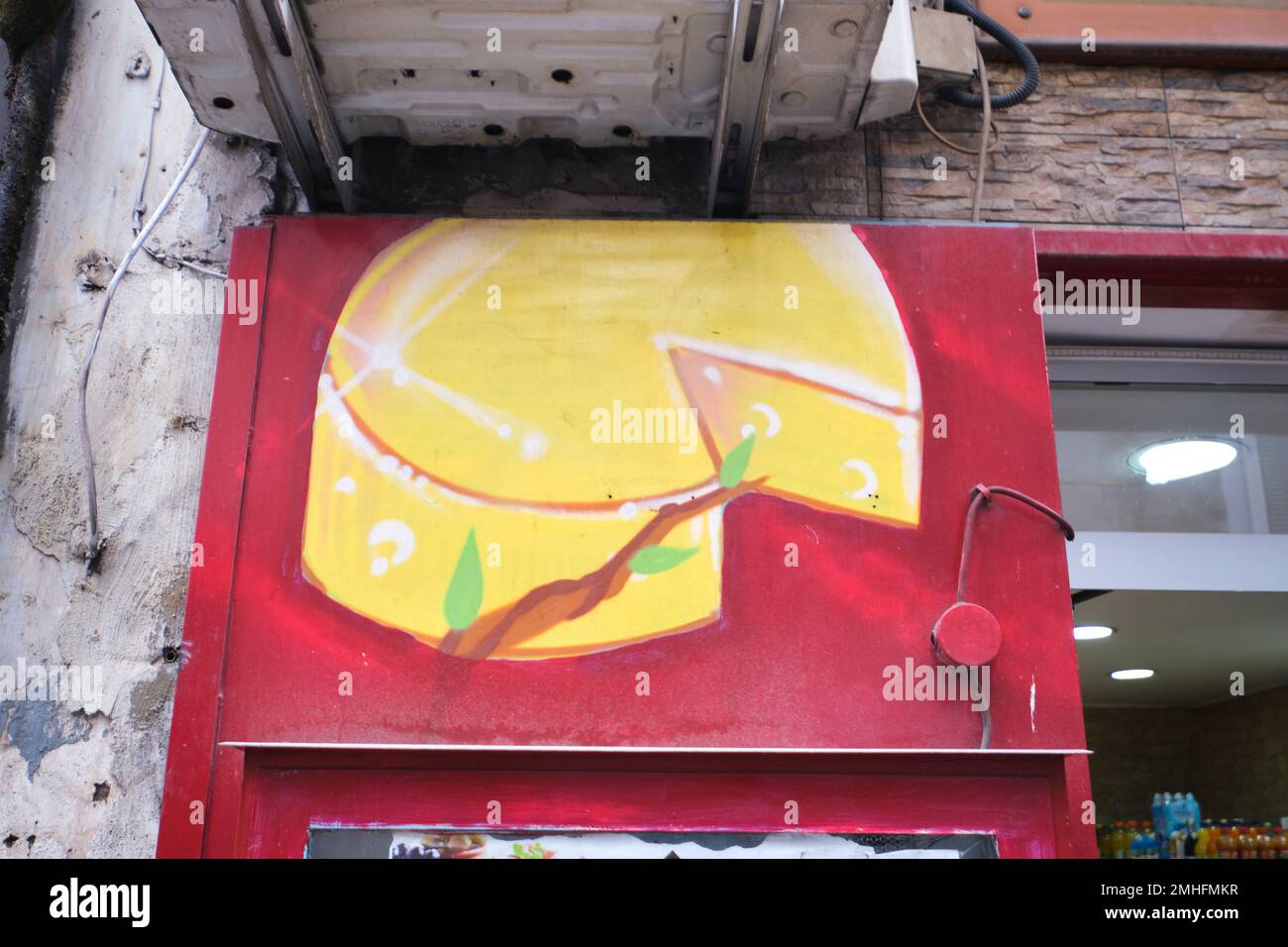 A detail on a local butcher shop of one of the handpainted illustrations of yellow wheel of cheese. An example of grafitti in Naples, Napoli, Italy, I Stock Photo