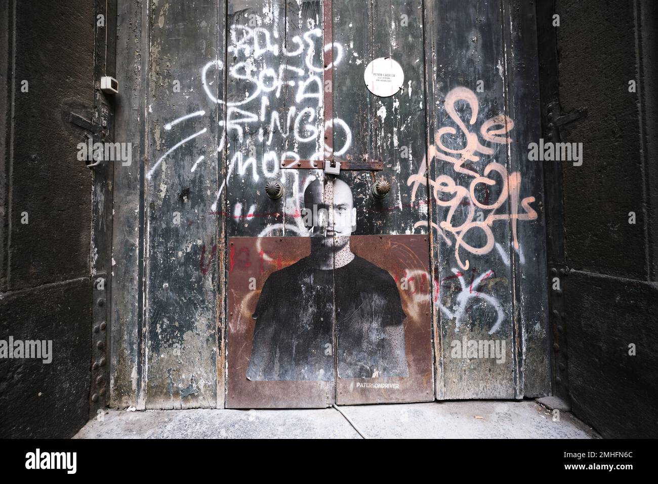 A paper poster stuck to the front door of an old building. The image is of a young man. An example of graffiti in Naples, Napoli, Italy, Italia. Stock Photo