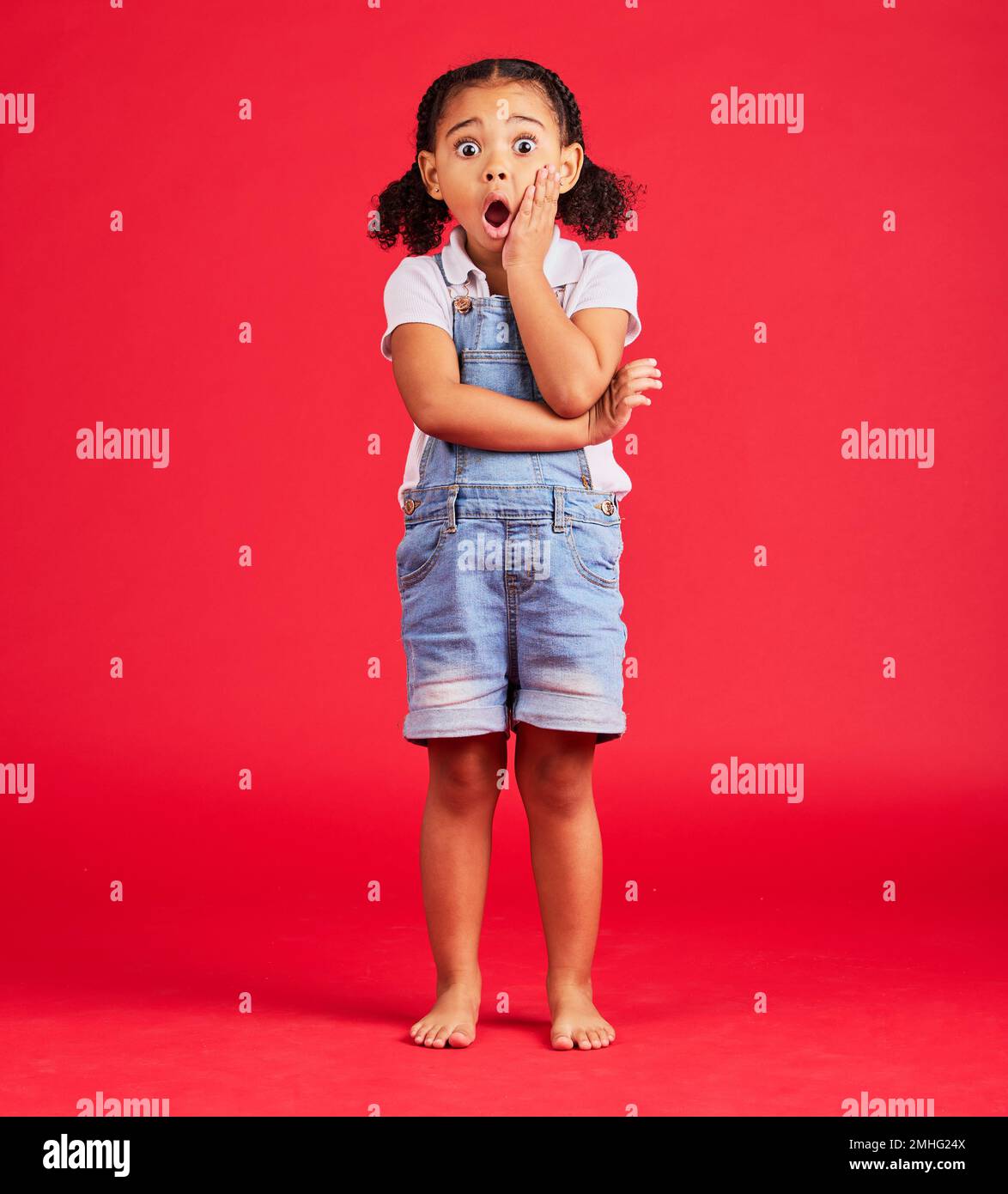 Little girl, portrait or shocked hand on face, isolated or red background and kids gossip, bad news or scary children story. Surprised, anxiety or Stock Photo