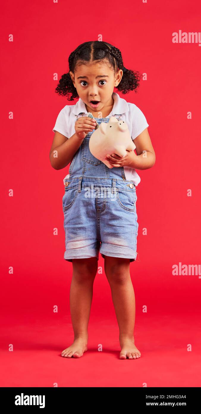 Surprised child, portrait and piggy bank for money deposit, kids savings or future investment on isolated red background. Shocked, girl and wow kid Stock Photo