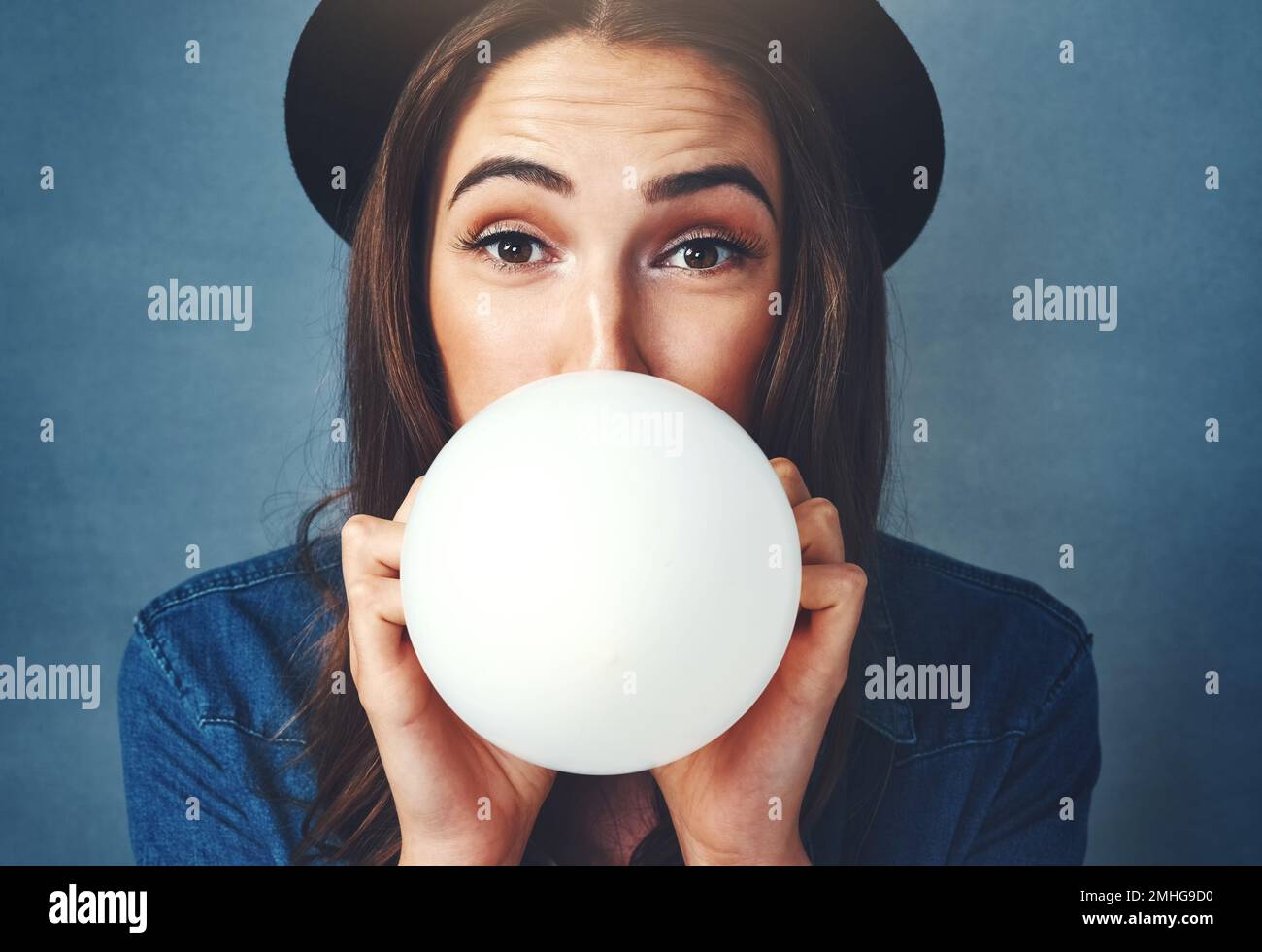 Its party time. Studio shot of an attractive young woman blowing up a balloon against a blue background. Stock Photo