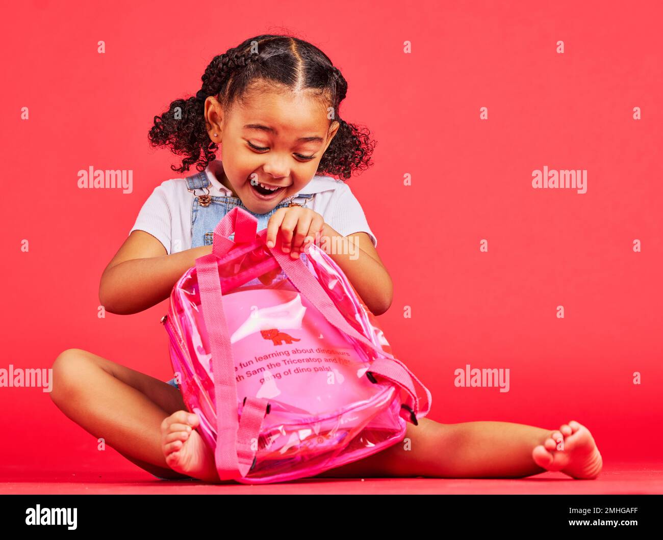 School, bag and red background with a student black girl in studio sitting on the floor against a wall. Children, education and excited with a female Stock Photo