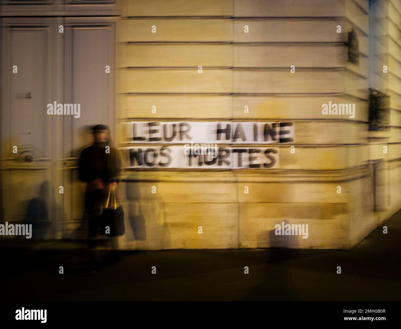 In this Nov. 8 2019 photo, Sarah stands next to slogan reading "Their hate,  our dead" in Paris. Under cover of night, activists have glued slogans to  the walls of buildings to