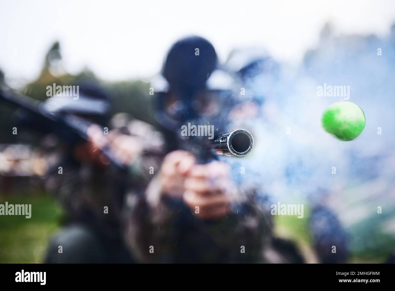 Paintball, shooting and person with a gun during a game, competition or match on a field. Fire, smoke and tool in motion for attack, battle and aim Stock Photo