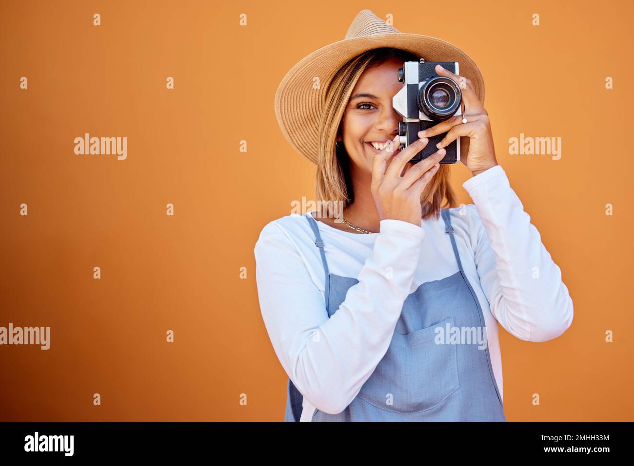 Photographer, portrait and woman shooting a picture or photo with a retro camera isolated in an orange background. Happy, studio and female taking Stock Photo