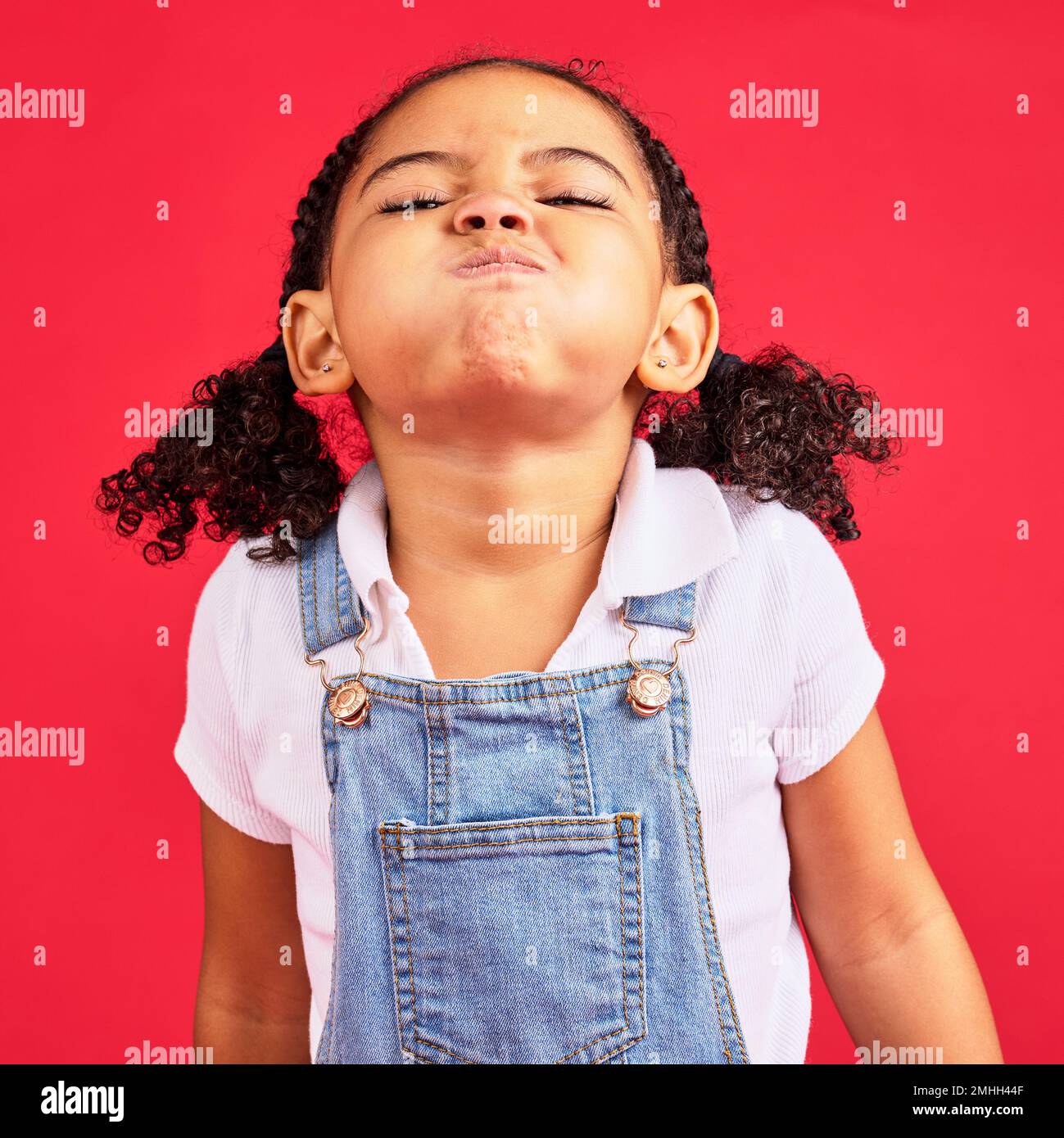 Attitude, childhood and face of girl on red background in studio with angry, upset and frustrated reaction. Emoji, comic and young kid with air in Stock Photo