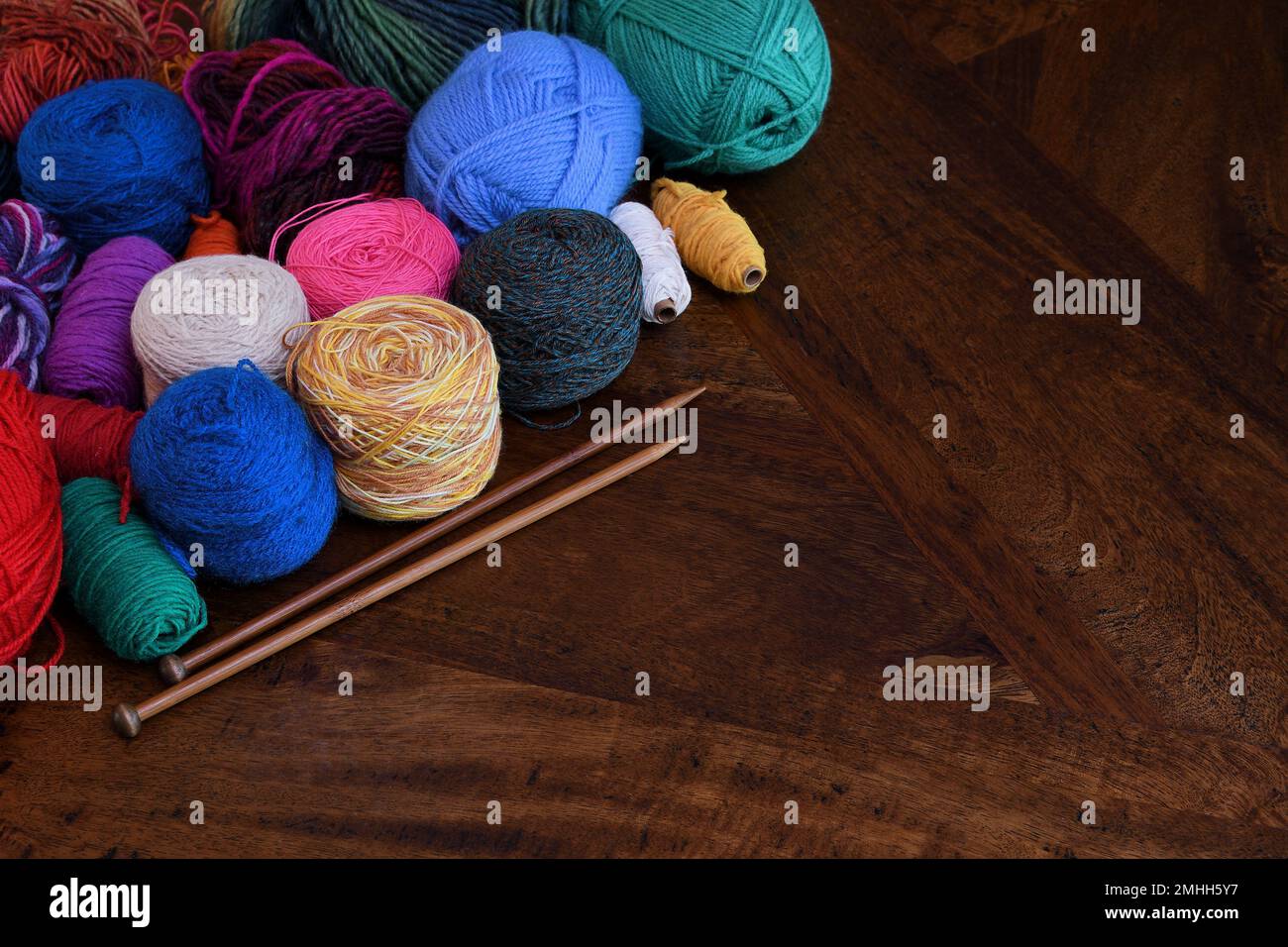 A montage pile of colourful balls of wool and wooden knitting needles in soft lighting with copy space to the right; captured in a studio Stock Photo