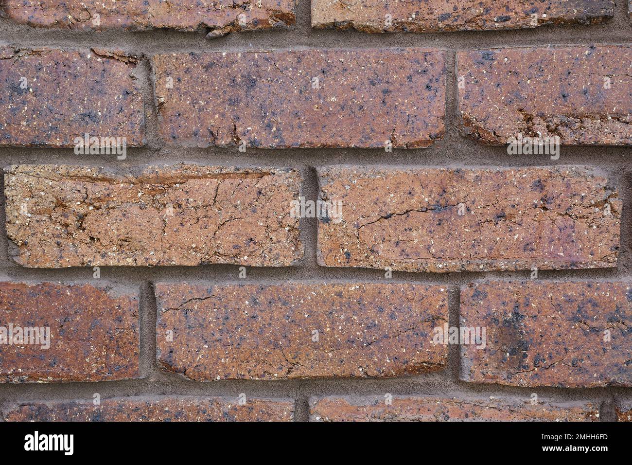 An extreme close-up view of a section of brownish, crimson coloured, coarse, rustic looking house bricks with vertical and horizontal joint lines Stock Photo