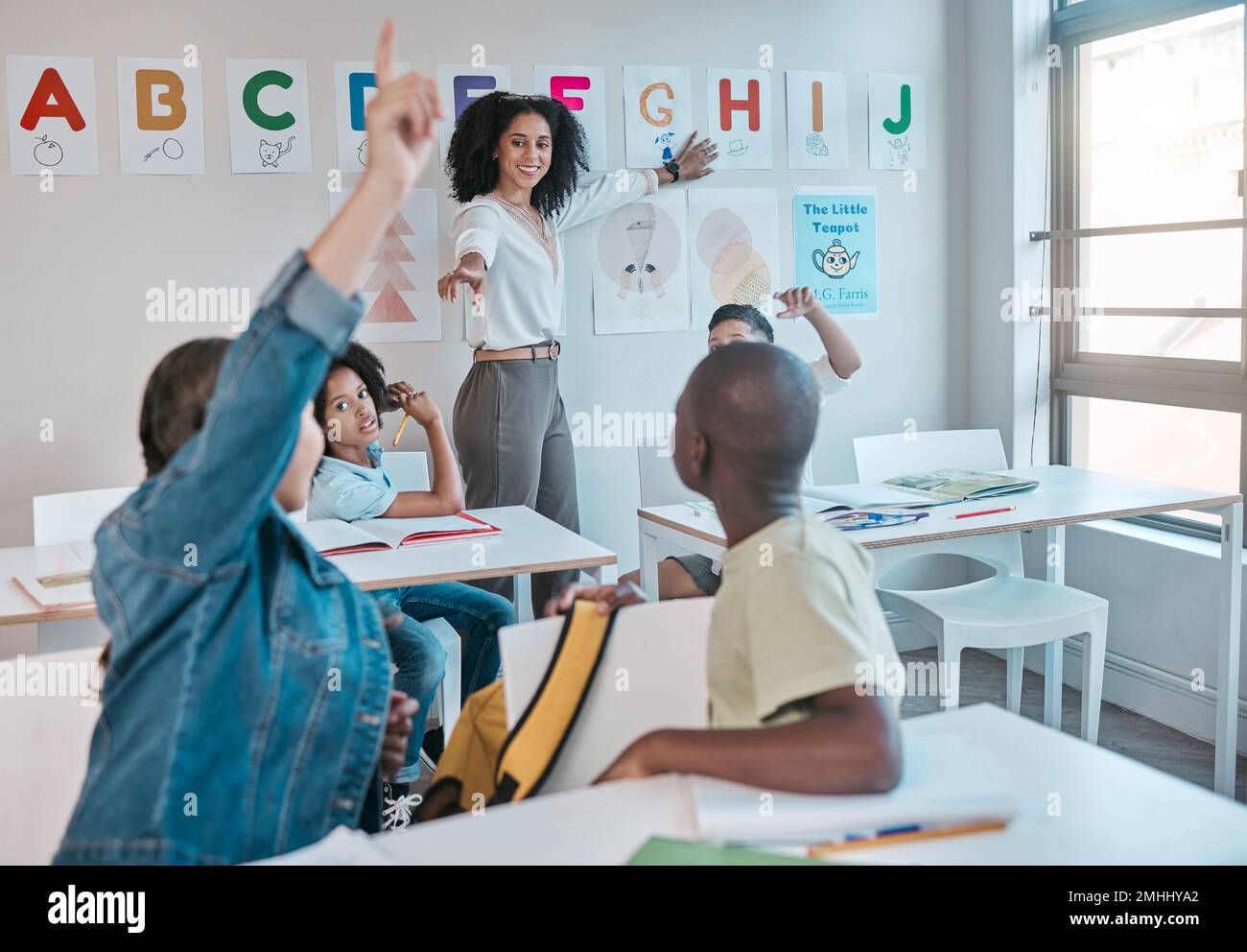 Teacher, question and woman happy for education and teaching at school with kids learning the alphabet and answer quiz. Raised hands, learners and Stock Photo