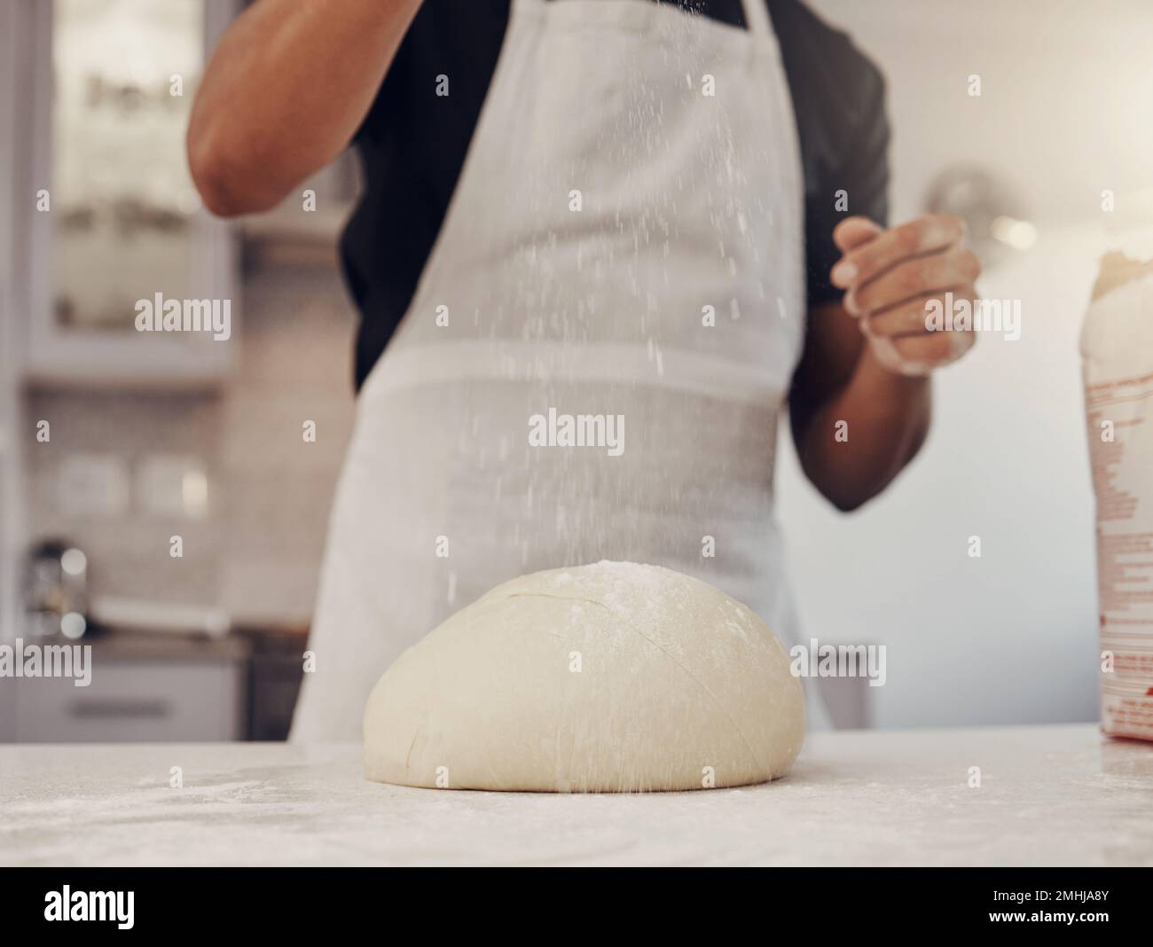 Chef man and flour sprinkle on dough for baking preparation work and process at culinary counter. Restaurant worker in professional kitchen preparing Stock Photo