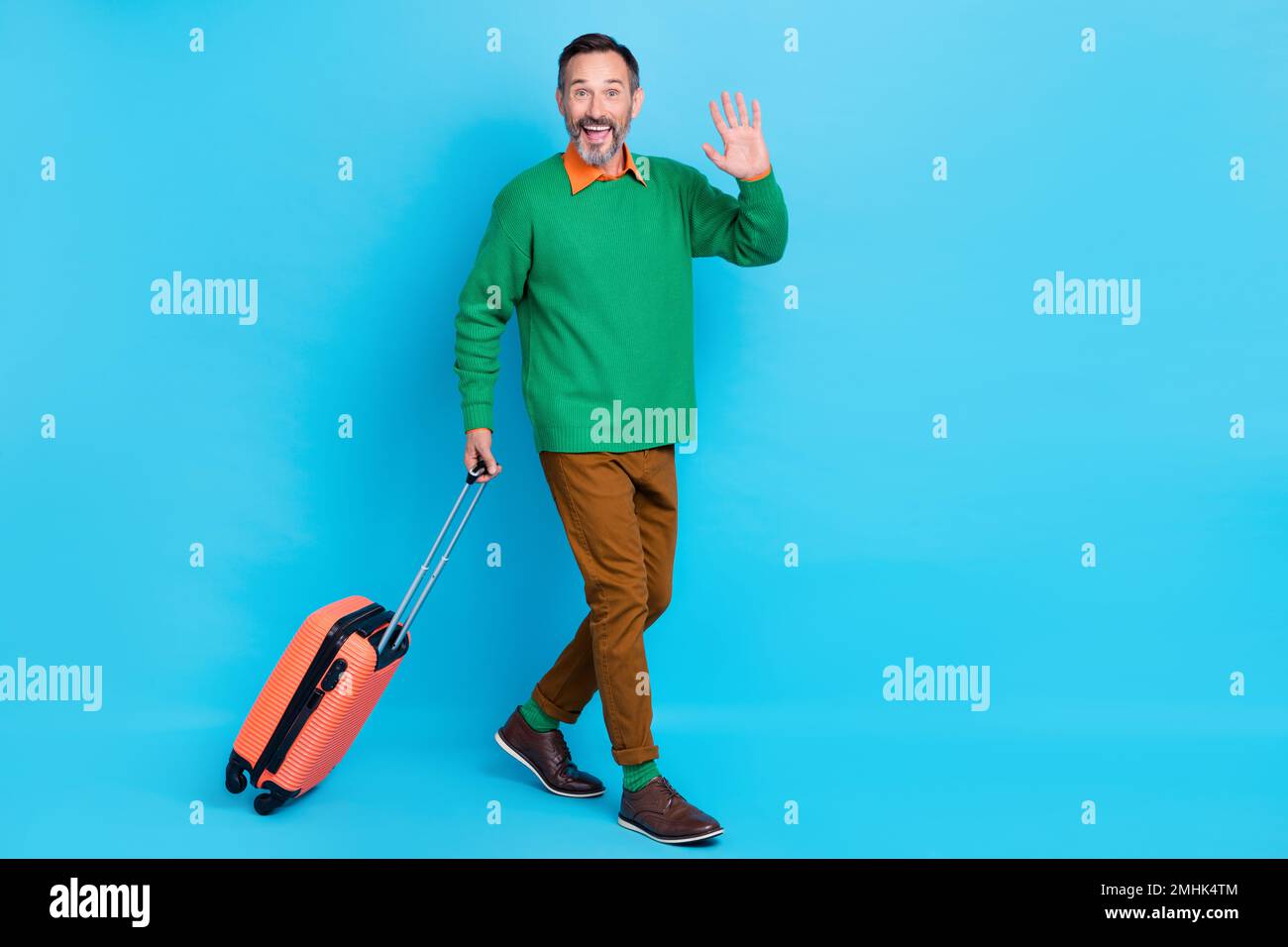 Full body photo of mature handsome man walking wave hand arrive hello dressed stylish green garment isolated on blue color background Stock Photo