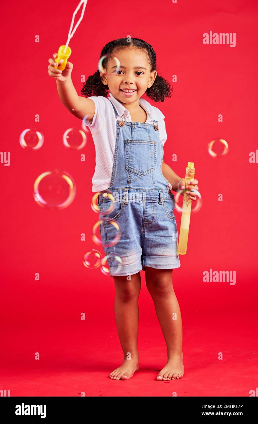 Child, portrait or bubbles playing on isolated red background in hand eye coordination, kids activity or fun game. Smile, happy or little girl and Stock Photo