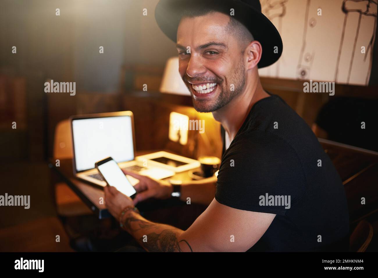 Hooked up to the net at my favourite hotspot. a young man using a phone and laptop while working in a coffee shop. Stock Photo