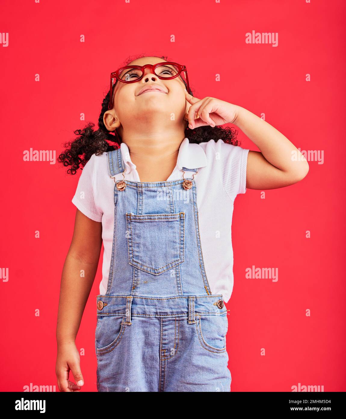 Looking up, thinking or child and fashion glasses on red background in vision, optician or eyesight sales deal. Smile, happy or little girl and Stock Photo