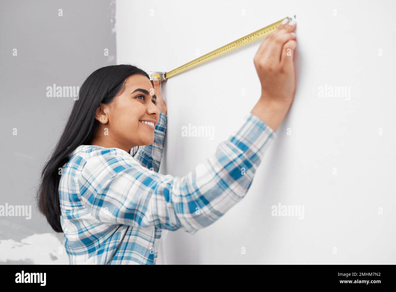 An Indian woman measures against the wall using measuring tape doing home DIY Stock Photo