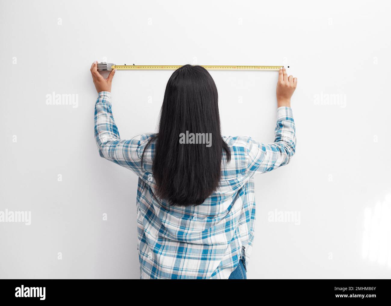 An Indian woman measures against the wall using measuring tape doing home DIY Stock Photo