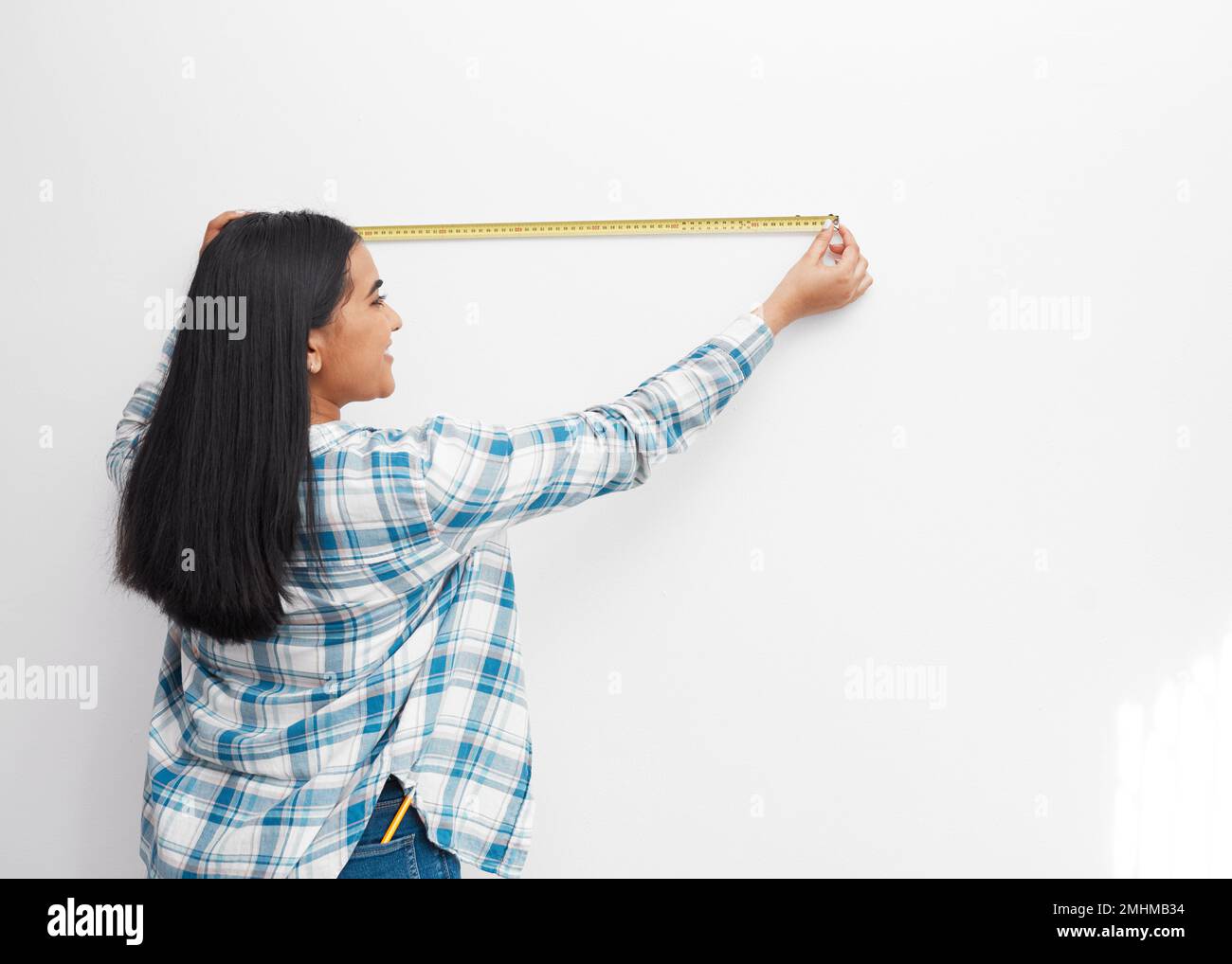 An Indian woman measures against the wall using measuring tape doing home DIY Stock Photo