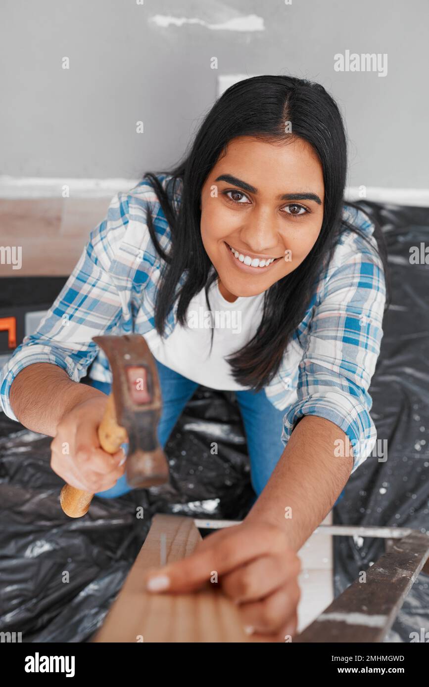 An attractive young Indian woman hammers a nail into wood home DIY