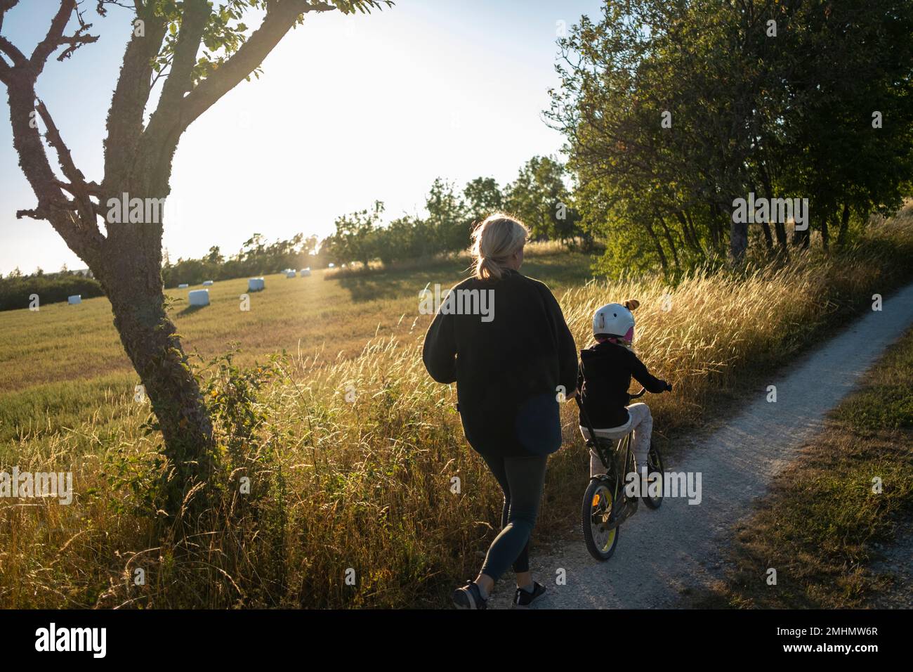 Mother teaching kid to ride bicycle on dirt road Stock Photo