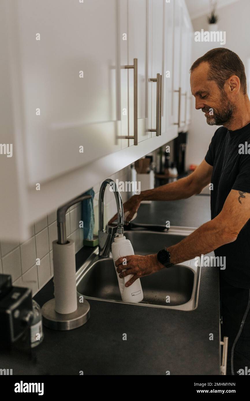 Man filling water bottle in kitchen Stock Photo Alamy