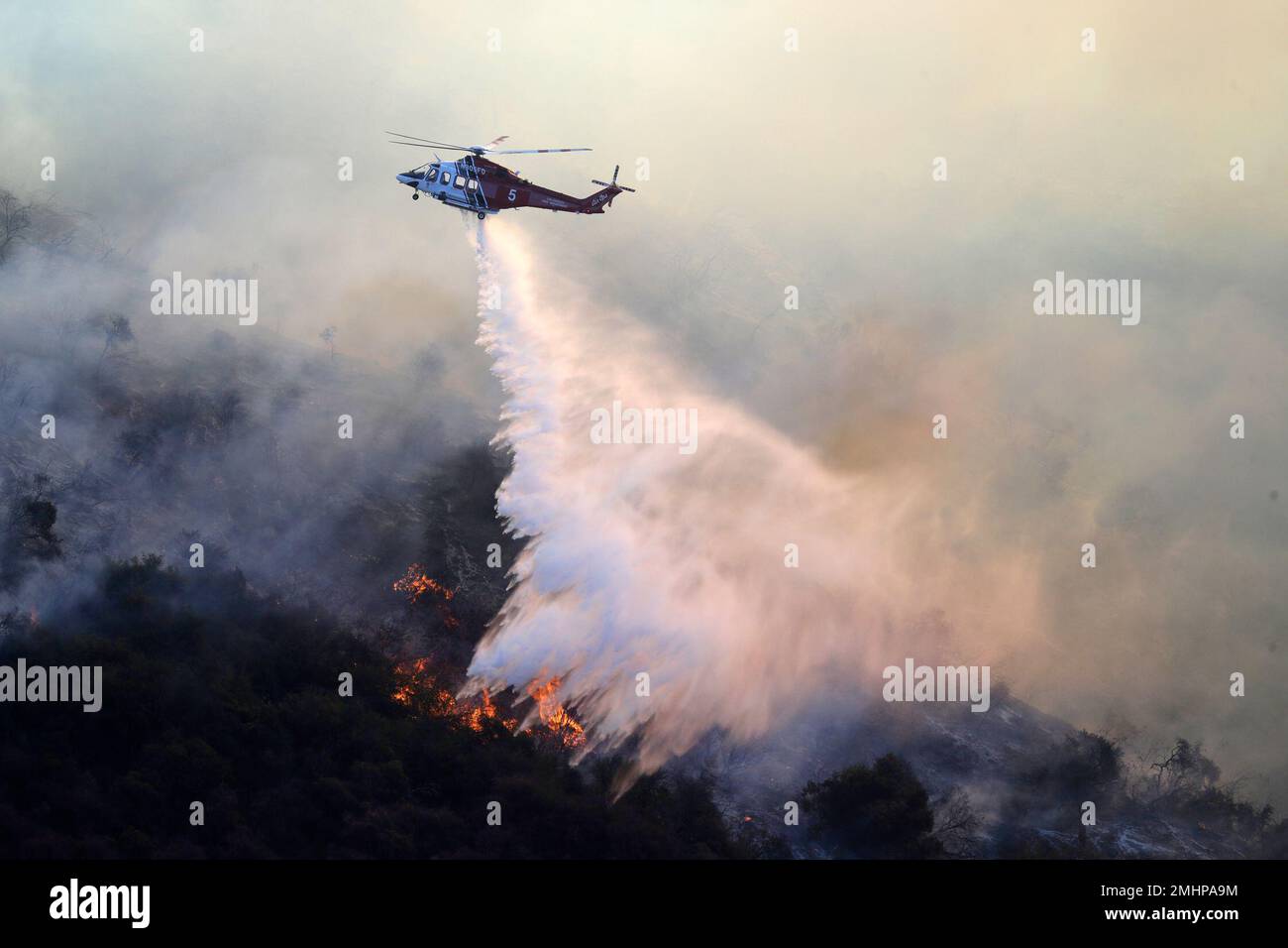 A helicopter drops water as the Getty fire burns on Mandeville Canyon