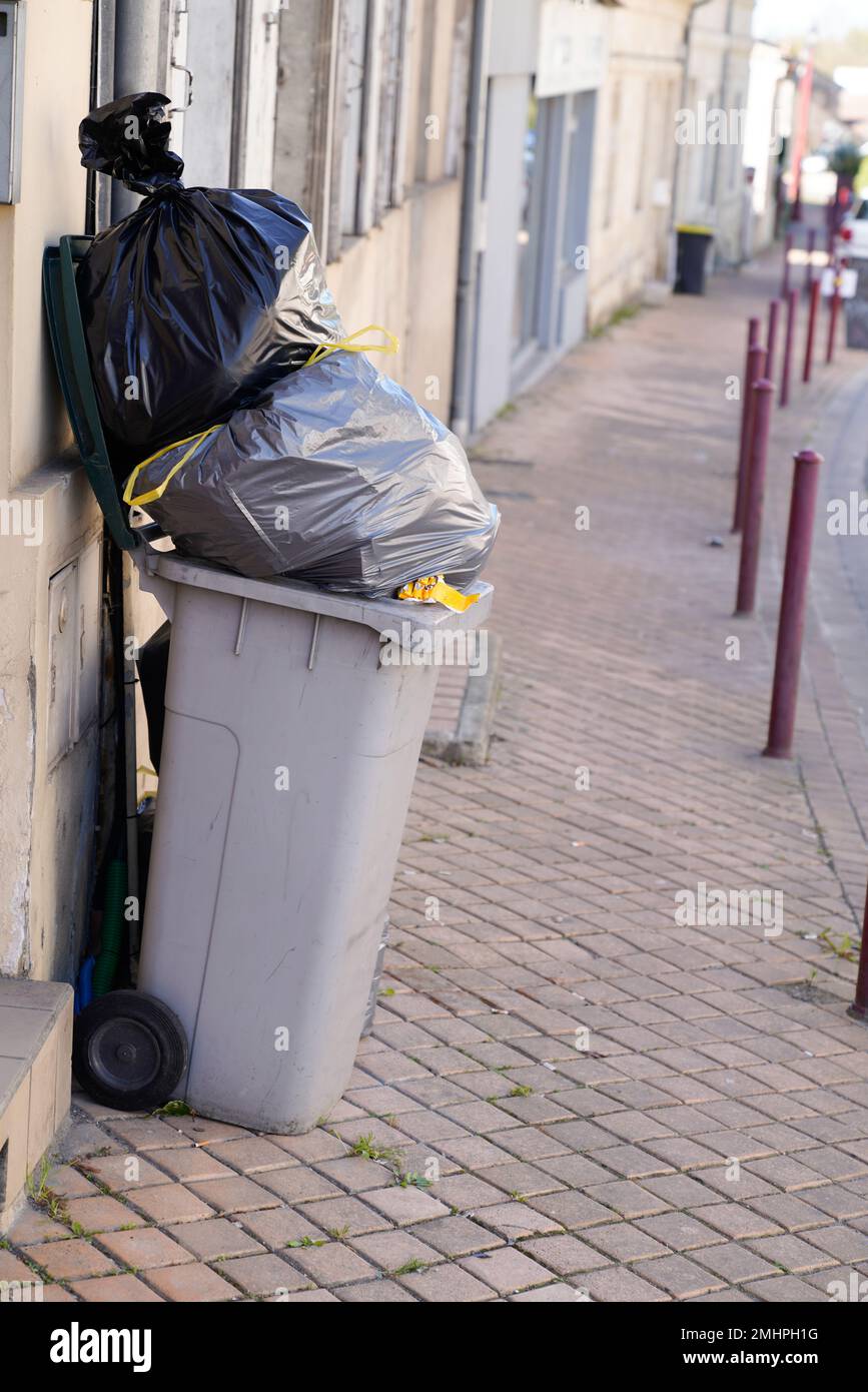 Rolling trash can overflowing bag grey wheelie in street city Stock