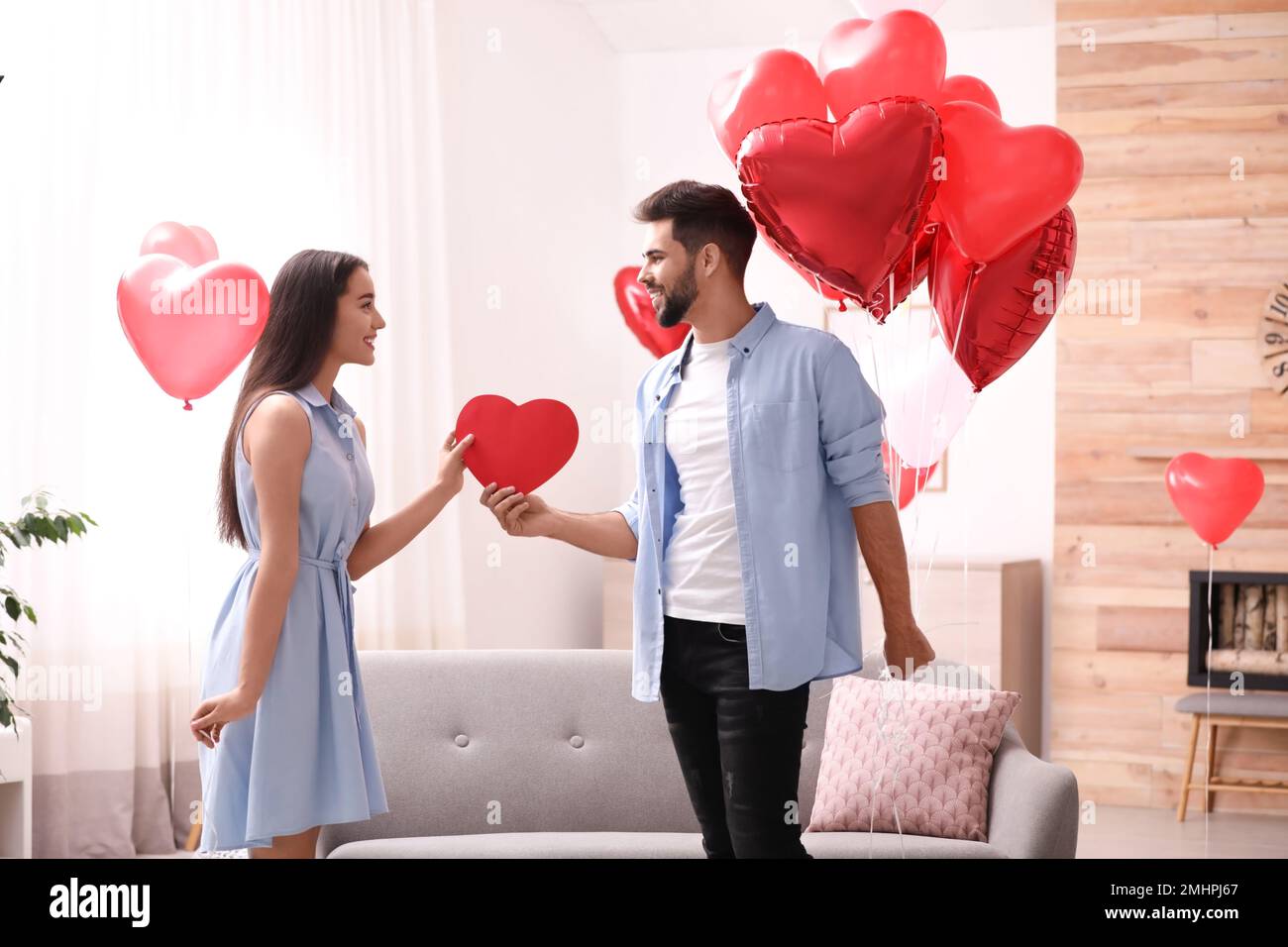 Lovely couple with heart shaped balloons in living room. Valentine's ...