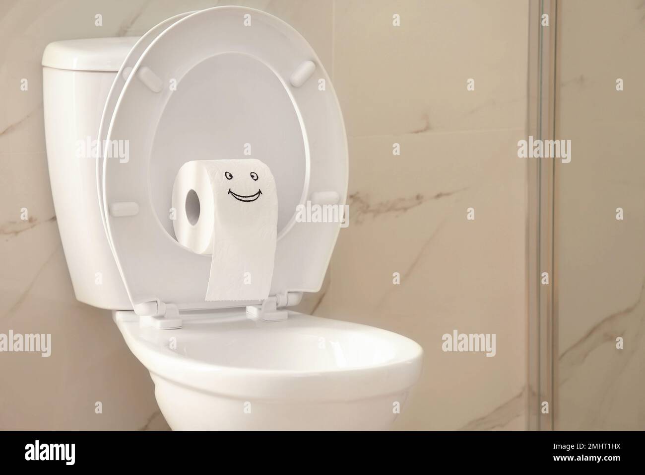 Roll of paper with funny face on toilet bowl in bathroom Stock Photo