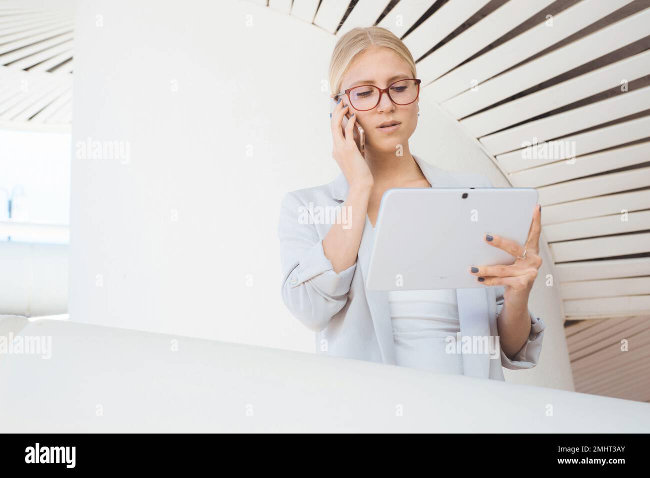 Young woman busy talking on the phone holding a white device Stock Photo