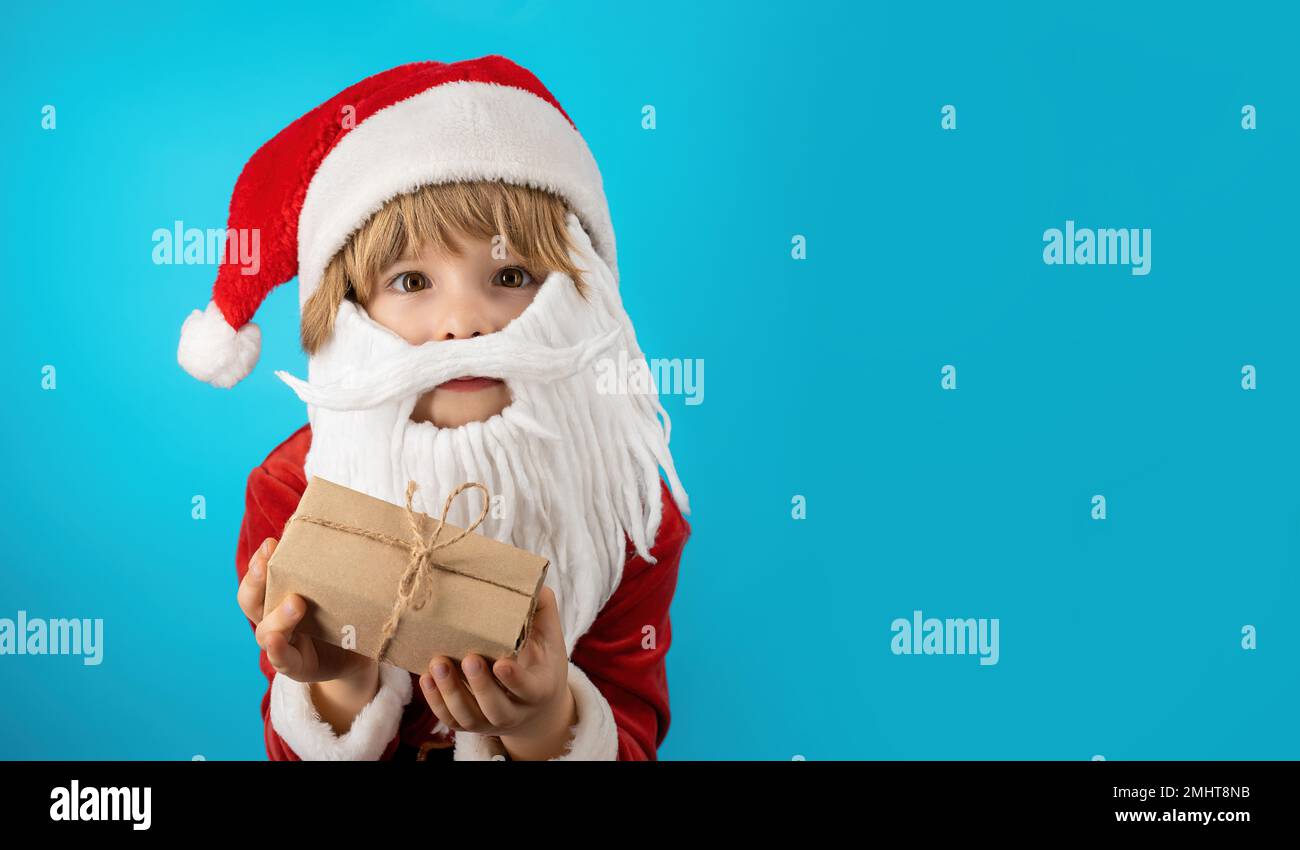 Excited boy in Santa costume with beard holding gift box with bow. Child, Happy kid with present. Blue Christmas background. Copy space, banner. High Stock Photo