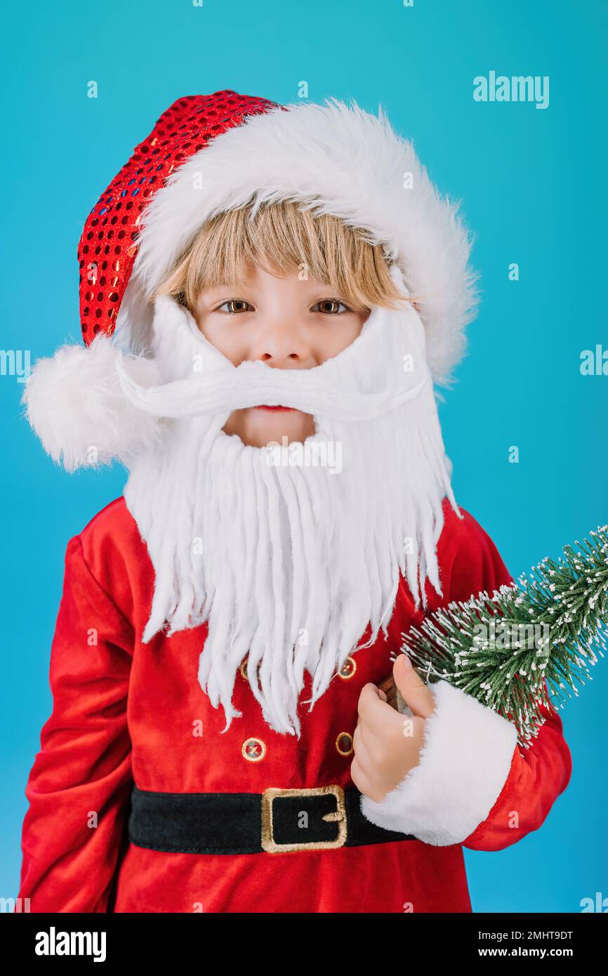 Friendly little Christmas boy in Santa Claus costume on blue background. Happy emotional child with artificial beard. High quality photo Stock Photo