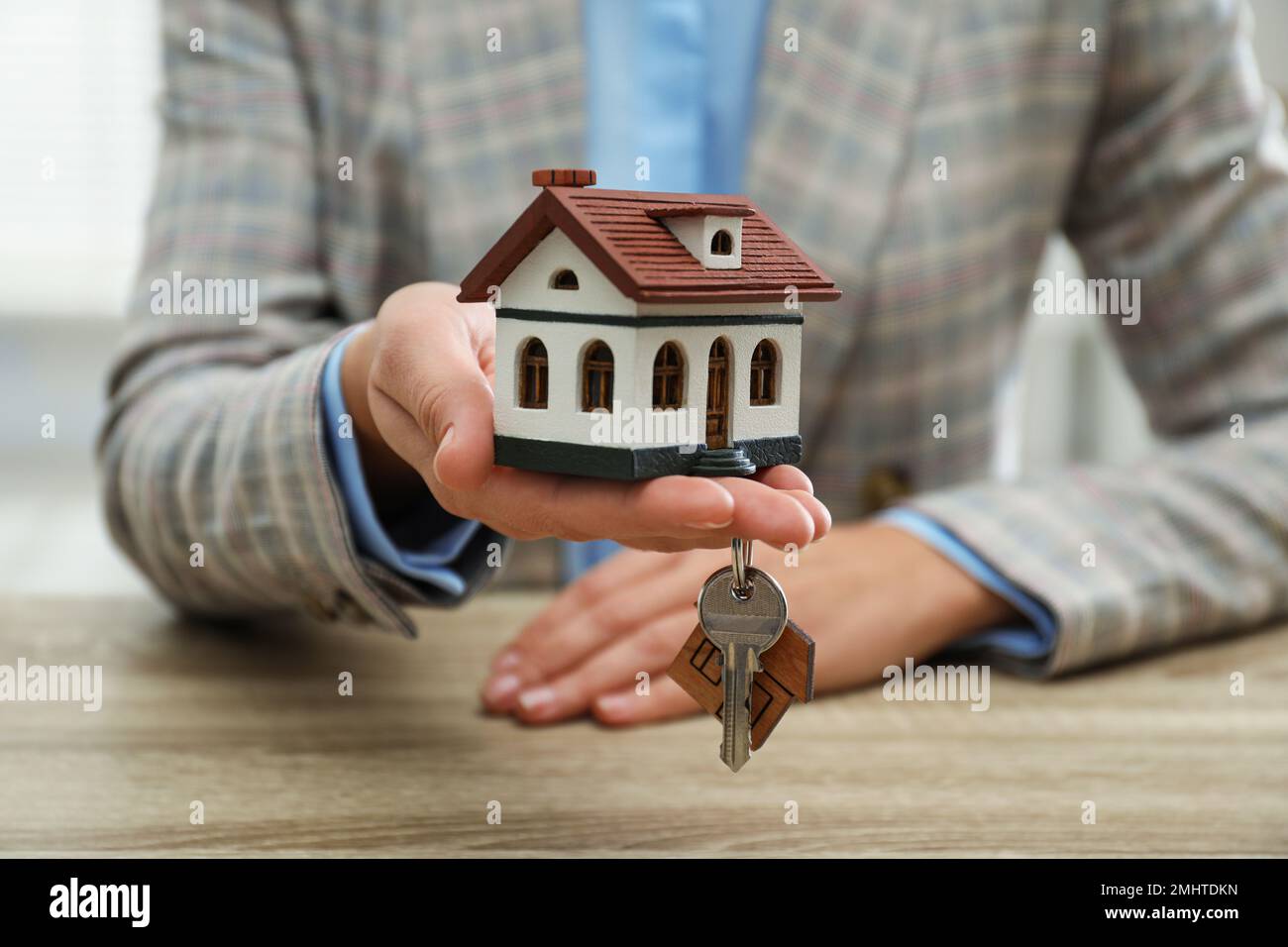 Real estate agent holding house model and key at wooden table, closeup ...